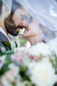 Bride and groom under veil about to kiss with flowers in forefront. Galveston wedding photography.